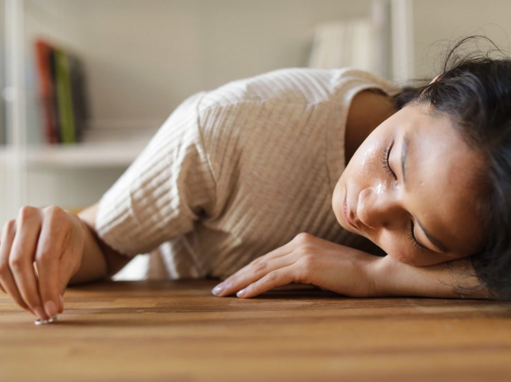 A Sad Woman Looking at the Ring she is Holding while Lying Her Face on a Wooden Surface